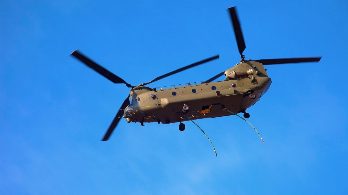 Tweemotorige Chinook-helikopter met draaiende rotors tegen een strakblauwe lucht.