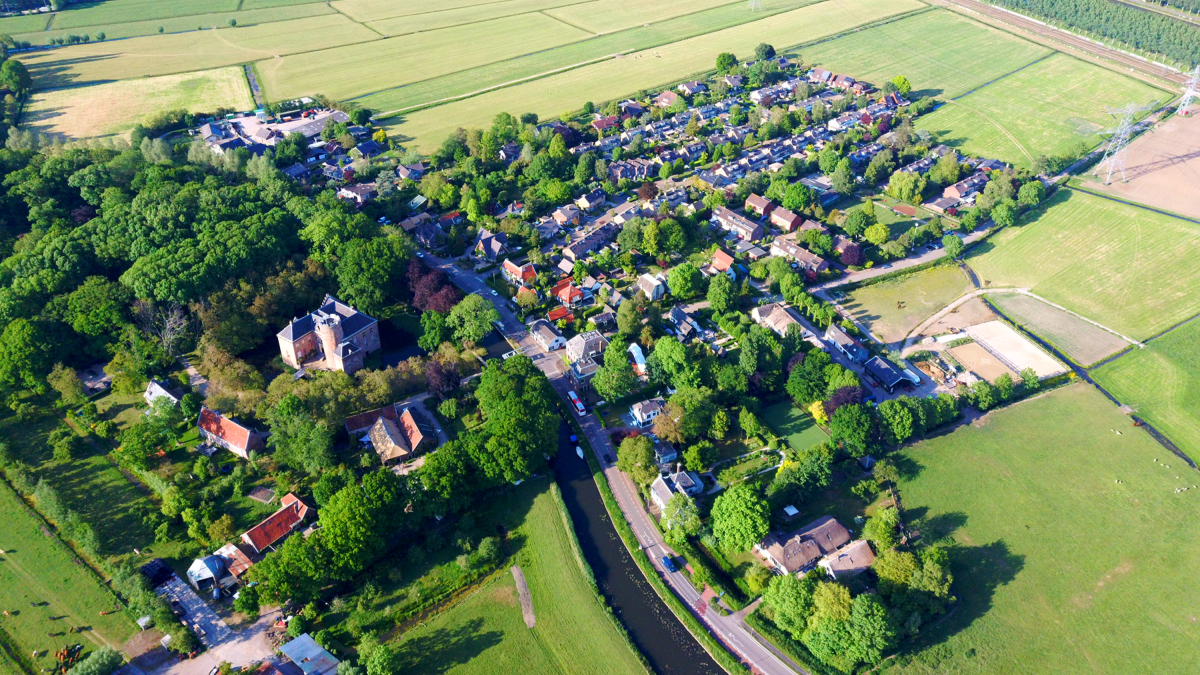 Luchtfoto van een dorp aan een vaart met een kasteel tussen de bomen