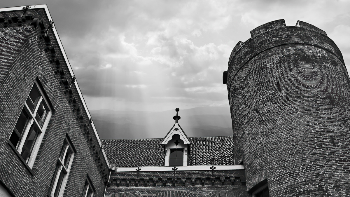 Oude gebouwen en kastelen – Zwart-witfoto van een kasteeltoren en bakstenen gevel onder een wolkenlucht