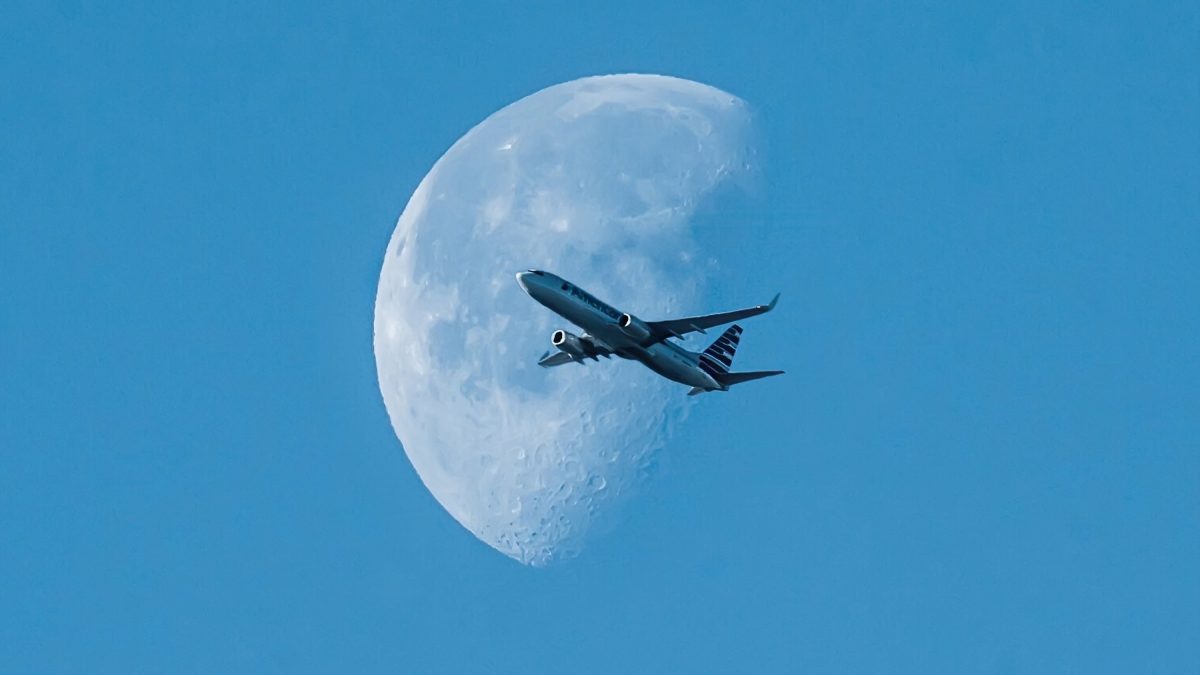Vliegtuig dat voor een gedetailleerde wassende maan vliegt in een heldere blauwe lucht
