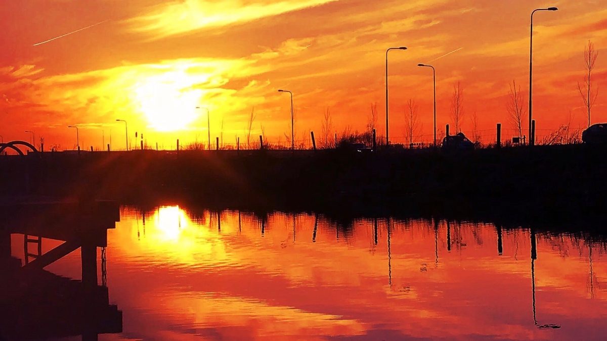Een vurige zonsondergang weerspiegelt in een waterplas langs de weg.